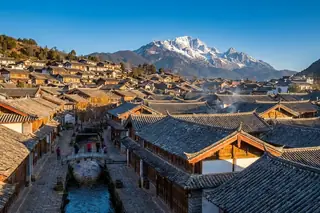 Lijiang, China — Dayan Old Town's grey-tiled Naxi rooftops and canals beneath the snow-capped Jade Dragon Snow Mountain