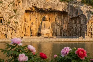Luoyang, China — the colossal cliff-carved Vairocana Buddha of the Longmen Grottoes above the Yi River with blooming peonies